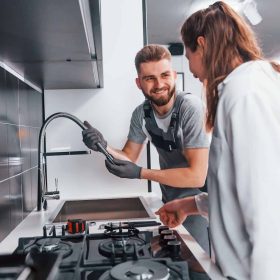 young-professional-plumber-in-grey-uniform-shows-results-of-work-for-housewife-on-the-kitchen.jpg